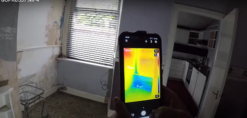Thermal imaging camera identifying cold moisture patches in a flood-damaged interior wall
